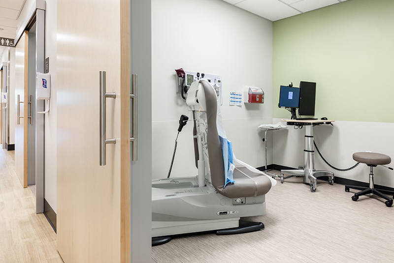Wood-toned sliding door used for an exam room door with healthcare equipment in the background.