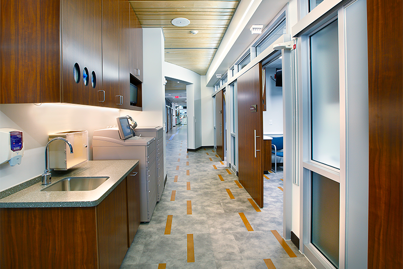 Hallway of a healthcare facility with sliding patient room doors and sink on the left.