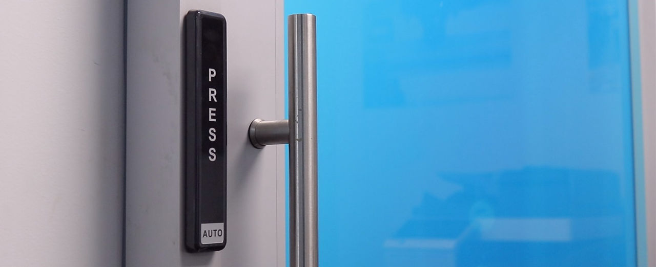 Automatic door with a modern push button, stainless steel handle, & blue glass panel. 