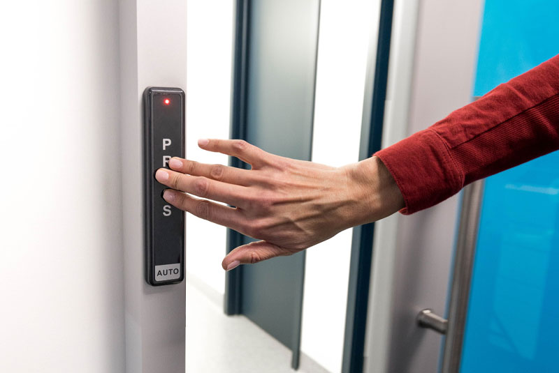 Close-up of a hand pressing a button to activate an interior automatic sliding door.