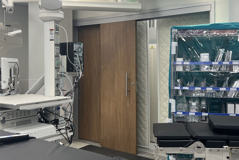 Telescoping sliding doors in a medical operating room, featuring a wood finish and heavy-duty frame to support flexible and accessible design.