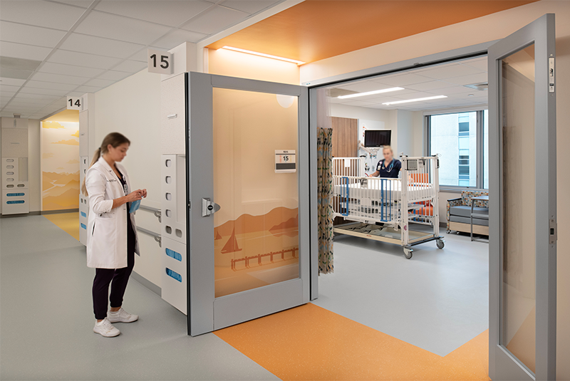 A medical professional beside an open dual swing door, ideally suited for flexible health care design, leads to a hallway and helps maximize clinic space.