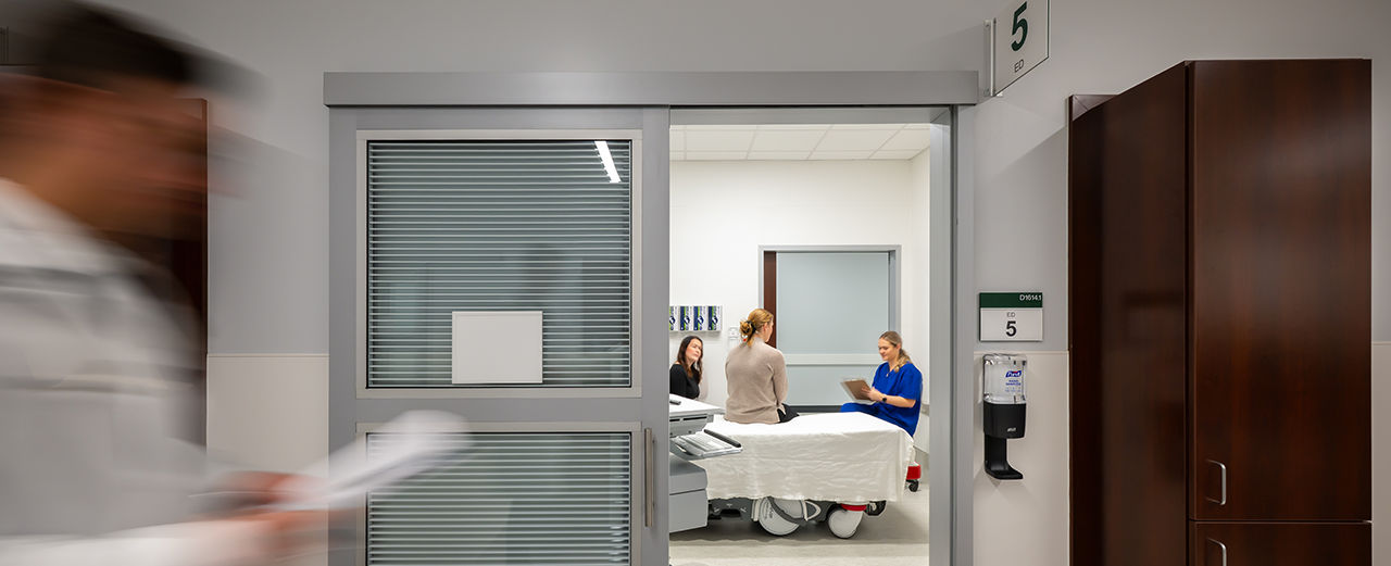 A doctor stands in front of a sliding glass door in a hospital room, showcasing flexible healthcare design.